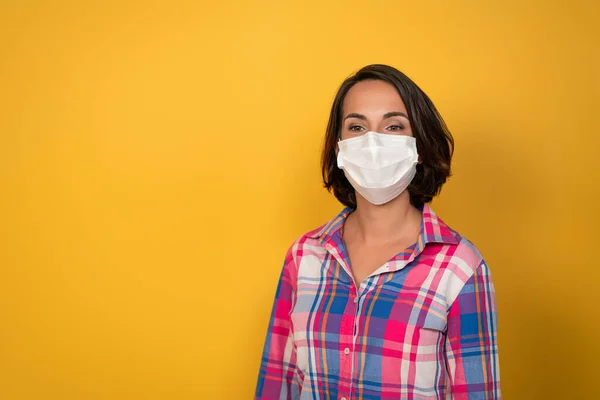 Mulher bonito vestindo máscara protetora branca isolado em fundo amarelo. Segurança durante uma pandemia, epidemia, gripe sazonal. Conceito de quarentena — Fotografia de Stock