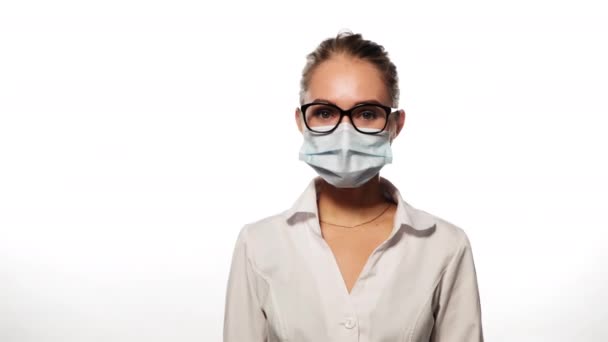 Jeune infirmière en lunettes et masque médical secouer la tête et écouter regarde la caméra. Isolé sur fond blanc. Images de haute qualité en résolution 4k — Video