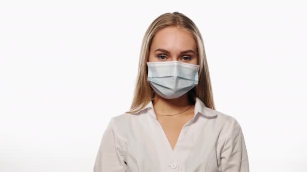 Die junge Krankenschwester in medizinischer Maske zeigt mit erhobenen Händen ein Liebeszeichen, blickt in die Kamera. Vereinzelt auf weißem Hintergrund. Hochwertiges 4k-Filmmaterial lizenzfreies Stockvideo