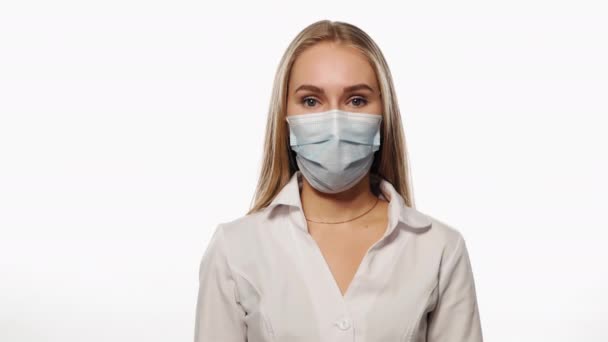 La giovane infermiera con una maschera medica annuisce come d'accordo, guarda la telecamera. Isolato su sfondo bianco. Filmati di alta qualità 4k risoluzione — Video Stock