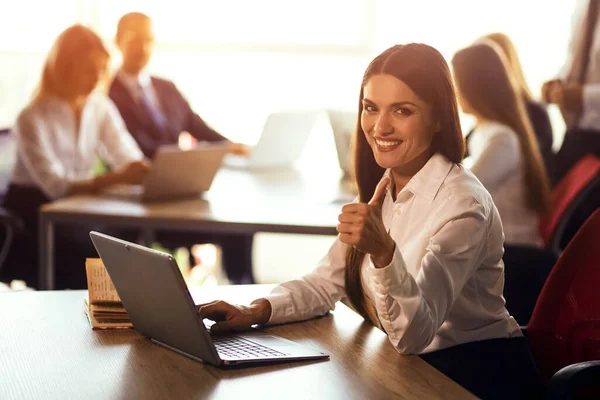 Joyeux jeune femme freelance travaillant sur ordinateur portable assis au bureau à aire ouverte ou coworking. Travailleuse travaillant sur une proposition d'entreprise ou développant des applications informatiques — Photo