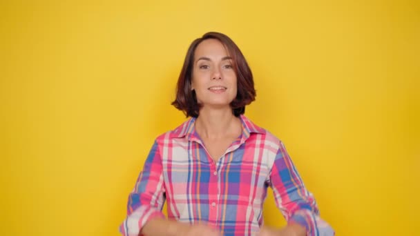 Portrait d'une jeune femme en chemise à carreaux à la mode montrant un symbole d'amour avec deux mains réunies dans le studio avec un sourire heureux. Plan intérieur d'une fille souriante heureuse isolée sur fond jaune — Video