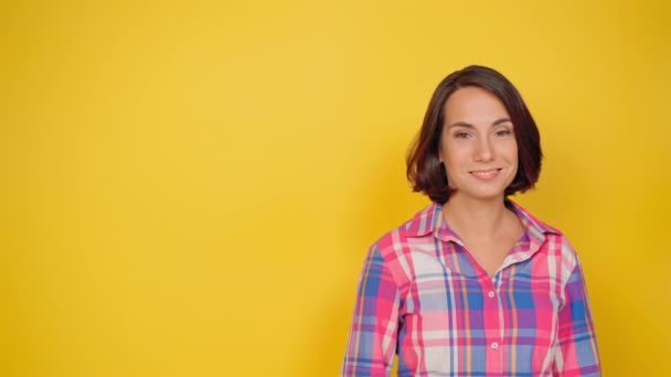 OK sign with one raised hand smile beautiful girl dressed in a plaid shirt and dark hair on a yellow background. Human emotions, facial expression concept. High quality 4k footage — Stock Video