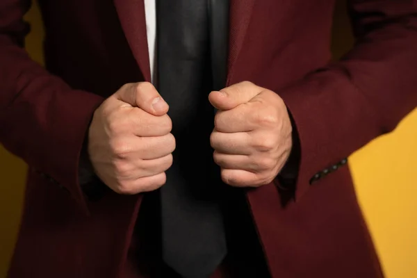 Gros plan sur les mains tenant un homme d'affaires veste bordeaux avec deux mains le fixant sur un corps isolé sur fond jaune — Photo