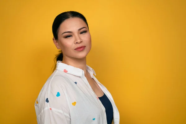 Charmante Aziatische vrouw aan de zijkant kijkend naar de camera, in casual wit shirt, geïsoleerd op gele achtergrond. Menselijke emoties, gezichtsuitdrukking concept — Stockfoto