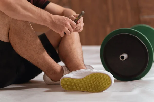 De cerca. Joven descansando sentado en el suelo con barra de fitness de tono negro y verde, equipo para el concepto de entrenamiento con pesas. Equipamiento deportivo masculino para entrenamiento. concepto de estilo de vida saludable — Foto de Stock