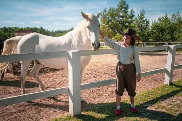 Jeune fille en vêtements vintage debout avec son cheval blanc vif dans le paddock à la journée ensoleillée. Image teintée. Concept d'amitié — Photo