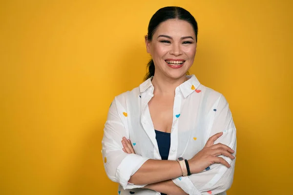 Heureuse femme asiatique regarde à la caméra, a le sourire aux dents, porte des vêtements décontractés et les bras repliés, isolé sur fond jaune. Émotions humaines, concept d'expression faciale — Photo