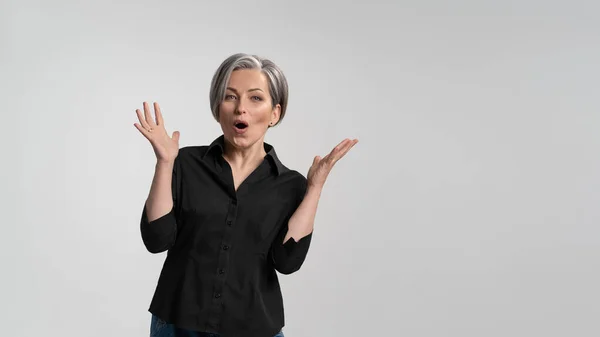 Grey haired mature woman doing a amazement gesture.Pretty mid aged grey haired woman in black shirt isolated on grey background. Human emotions, facial expression concept — Stock Photo, Image