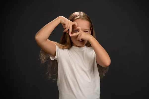 Love gesture happy 8,10 years old girl holding her hands together making a heart shape and looking thru it wearing white t shirt smiling at the camera isolated on dark grey or black background — Stock Photo, Image