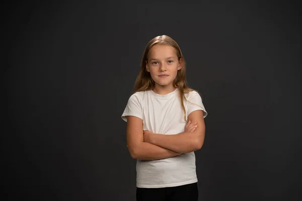 Kleines Mädchen von 8,10 Jahren mit gefalteten Händen blickt fragend in die Kamera, trägt weißes T-Shirt auf dunkelgrauem oder schwarzem Hintergrund — Stockfoto