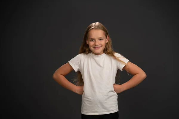 Bossy kleine Mädchen von 8,10 Jahren legte ihre Hände zur Seite schaut fragend in die Kamera trägt weißes T-Shirt isoliert auf dunkelgrauem oder schwarzem Hintergrund — Stockfoto