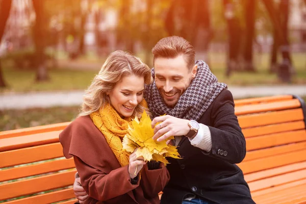 Ein junges, glückliches romantisches Paar, das sanft umarmt auf einer Bank im Park sitzt und Mäntel und Schals trägt. Ein romantisches Paar, das sich auf einer Bank im Park umarmt. Liebesgeschichte — Stockfoto