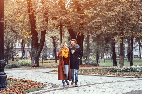 Manželé se procházejí v podzimním parku s roztomilým objetím. Venkovní záběr zamilovaného mladého páru kráčejícího po stezce podzimním parkem. Tónovaný obrázek — Stock fotografie