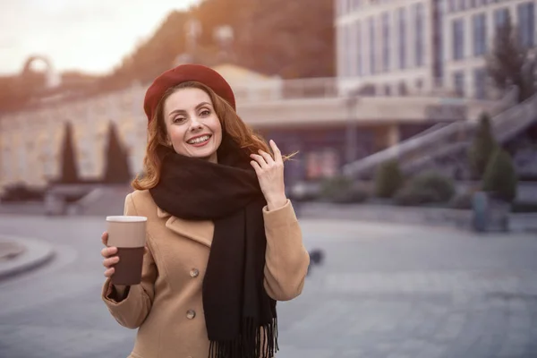 Alkalmi portré francia nő kezében kávésbögre kívül ősszel bézs kabát és piros sapka városi háttérrel. Színes fénykép — Stock Fotó