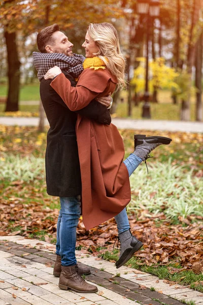 Esposo levantando una esposa se abrazó riendo en el parque de otoño con un lindo abrazo. Foto al aire libre de una joven pareja enamorada pasándola muy bien abrazándose en un parque de otoño. Imagen teñida — Foto de Stock