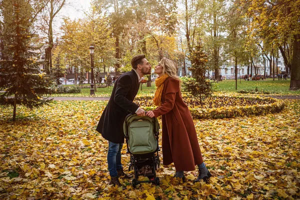 Família caminhando em um parque de outono com um bebê recém-nascido em um carrinho de bebê. Família ao ar livre em um parque de outono dourado. Imagem matizada — Fotografia de Stock