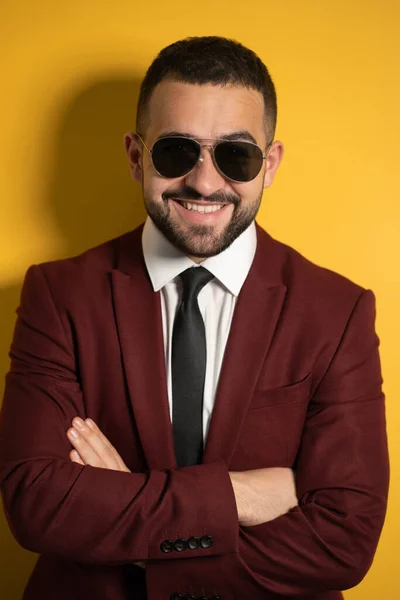 Close up portrait of handsome business man in sunglasses and burgundy suit looking at camera with hands folded isolated on yellow background — Stock Photo, Image