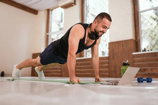 Ung sportsmand gør op push ups motion i tomme gym eller hjemme at se online sportsvideoer. Muskelsportsmand gør øvelser alene, mens self distance eller lockdown i gymnastiksalen - Stock-foto