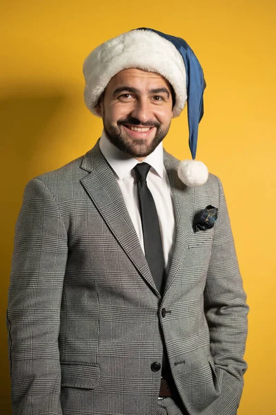 Ung vacker skäggig leende Santa man bär blå jultomte hatt och kostym, tittar på kameran isolerad på gul bakgrund. Positiva känslor, ansiktsuttryck, känslor säsongsbetonad semester — Stockfoto