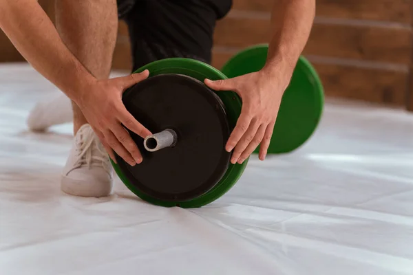 Opsætning af en vægtstang ung mand bue på et knæ tilføje en sort og grønne plader, udstyr til vægttræning koncept. Sportsudstyr til træning. Vægttab, sund livsstil koncept - Stock-foto