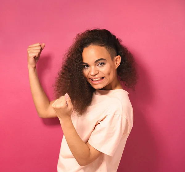 Šťastná krásná mladá Afroameričanka dívající se pozitivně na kameru s broskvovým tričkem ukazujícím svaly izolované na růžovém pozadí. Krása konceptu — Stock fotografie