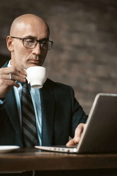 커피를 마시고 있는 성인 사업가가 노트북 컴퓨터를 하고 있고 테이블에 앉아 안경 안경을 쓴 노트북을 보고 있습니다. 사업 개념 — 스톡 사진