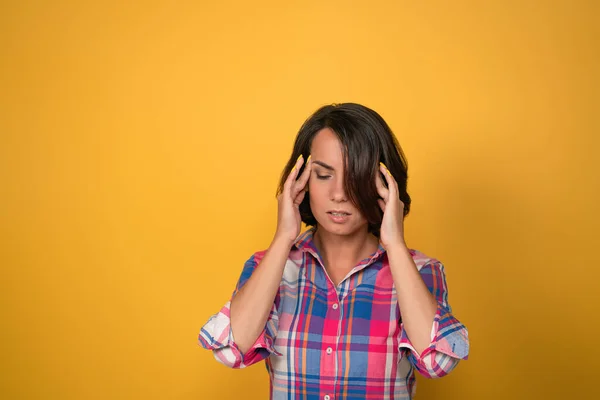 Eine kopfschmerzgeplagte Frau, die versucht, mit Migräne fertig zu werden, die nach unten schaut, während sie vor der gelben Wand im Hintergrund mit Kopierraum steht — Stockfoto