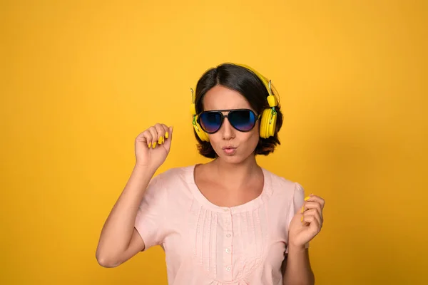 Молода красива леді в персиковій футболці слухає музику в навушниках і сонцезахисних окулярах, танцюючи ізольовано на жовтому фоні. Музична концепція. Технологічна концепція. концепція моди — стокове фото