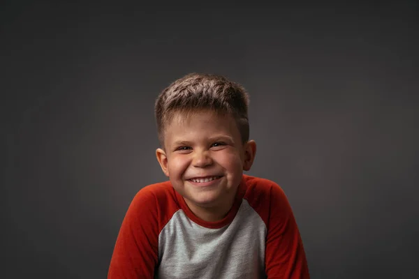 Gros plan d'un petit garçon qui sourit joyeusement devant une caméra isolée sur fond gris foncé ou noir. Images de portrait de jeune garçon sur noir. Images haute définition — Photo