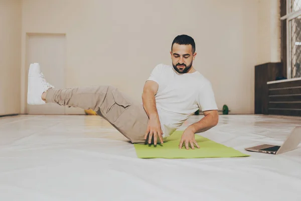 Bajo ángulo. Joven hombre guapo haciendo crujidos y buscando videos de ejercicios en línea sobre el uso de la computadora portátil. Auto motivado joven calentamiento haciendo ejercicios especiales para los músculos abdominales — Foto de Stock