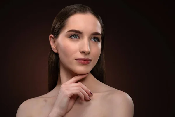 Nenhum retrato de maquiagem de uma mulher bonita com um cabelo longo e ombros nus. Menina modelo morena encantadora posando na câmera tocando seu queixo com um dedo isolado no fundo preto — Fotografia de Stock