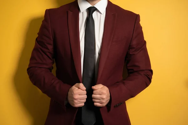 No head close up shot pf a hands holding a business man burgundy color jacket with two hands fixing it on a body isolated on yellow background — Stock Photo, Image