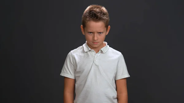 Gonosz kisfiú néz a kamera fehér póló és fekete nadrág elszigetelt fekete háttér — Stock Fotó