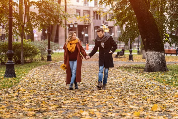 Paar, das Händchen haltend im Park spaziert. Außenaufnahme eines jungen verliebten Paares, das auf einem Pfad durch einen herbstlichen Park spaziert. Herbstliches Image — Stockfoto