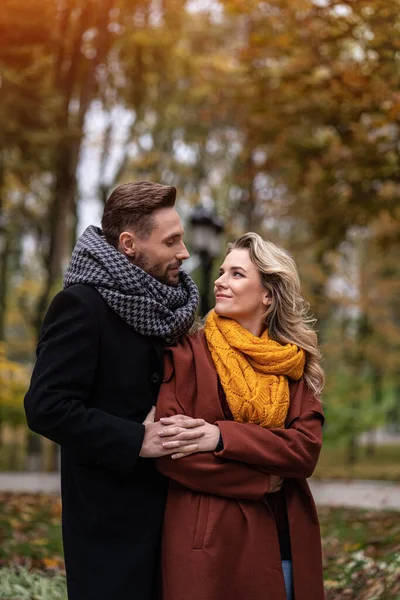 Bonito homem e uma mulher abraçados por trás sorriem olhando um para o outro no parque de outono. Tiro ao ar livre de um jovem casal apaixonado ter grande momento. Imagem tonificada de outono — Fotografia de Stock