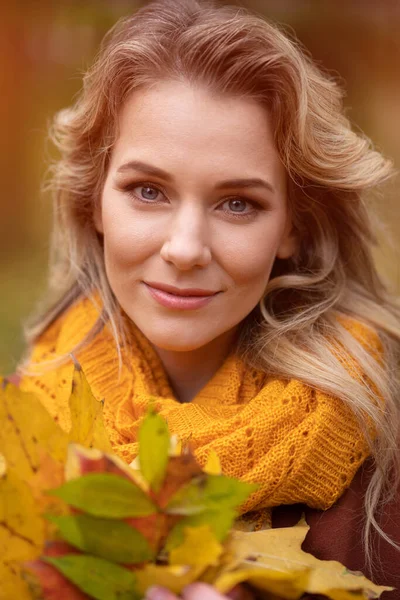 Giovane donna affascinante in posa con foglie cadute ingiallite per la fotocamera con camminare intorno giardino giallo autunno o parco. Bella giovane donna sorridente in foglie di autunno — Foto Stock