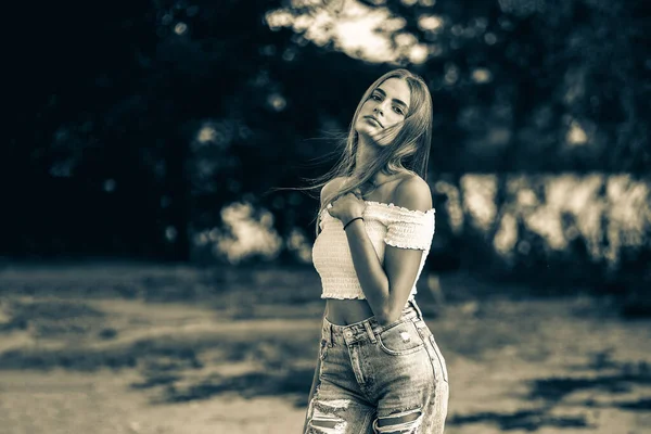 Красивая девушка-подросток в белых обнаженных плечах и джинсах, позирующих против деревьев на размытом природном фоне на берегу реки. Черно-белое изображение — стоковое фото