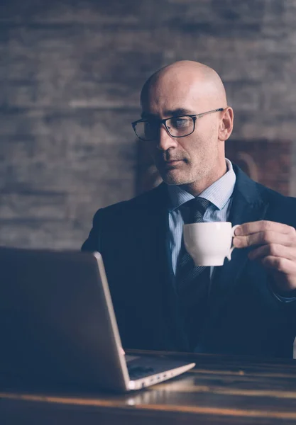 한 사업가가 휴식 시간에 커피를 마시면서 업무 서신을 확인하고는 손에 커피 한 잔을 들고 안경을 쓴 노트북 모니터를 들여다 봅니다. 사업 개념. 연결 된 이미지 — 스톡 사진
