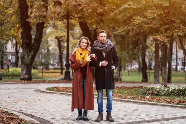 Fullständigt porträtt av ett par på en date promenader i höstparken med händerna. Utomhus foto av ett ungt par kär promenader längs en stig genom en höstpark — Stockfoto