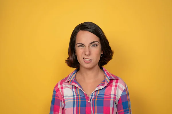 Hesitação olhar de uma jovem posando na câmera. Mulher de camisa xadrez em fundo amarelo. Emoções humanas, conceito de expressão facial — Fotografia de Stock