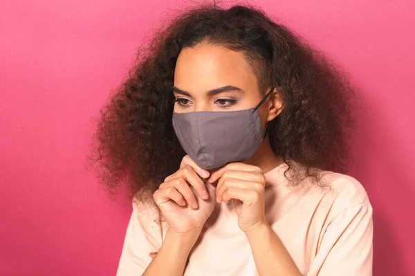 Colocar uma máscara facial reutilizável jovem afro-americana em camiseta pêssego claro, para evitar que outros de corona COVID-19 e SARS cov 2 infecção isolada em fundo rosa — Fotografia de Stock