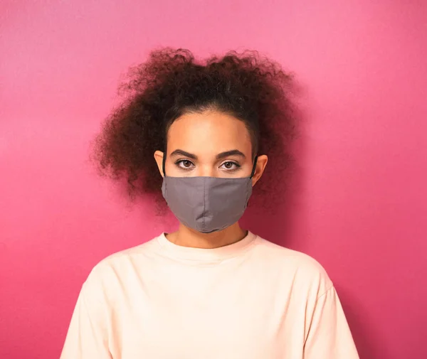 Bela fêmea afro-americana em máscara facial reutilizável vestindo camiseta pêssego claro, para evitar que outros de corona COVID-19 e SARS cov 2 infecção isolada em fundo rosa. Imagem quadrada — Fotografia de Stock