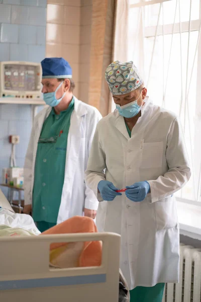 Двоє чоловіків-лікарів відвідують пацієнта і приписують медичне лікування. Лікарі у відділенні реанімації. Міська лікарня. Травень 2020, Броварі, Україна — стокове фото