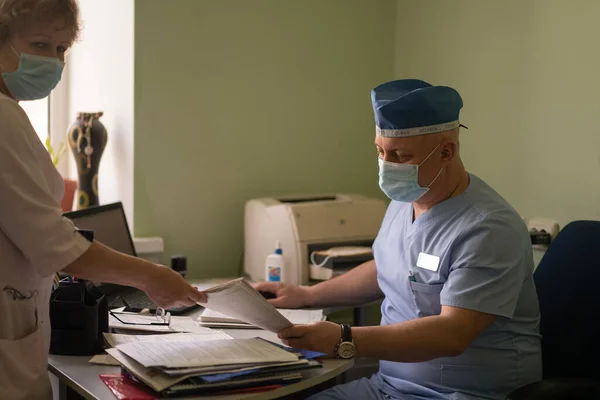 O médico chefe que fala com a enfermeira trabalha com a aplicação do doente. Homem GP em uniforme de proteção com trabalhar com documentos em seu escritório. Hospital da cidade. Maio, 2020, Brovary, Ucrânia — Fotografia de Stock