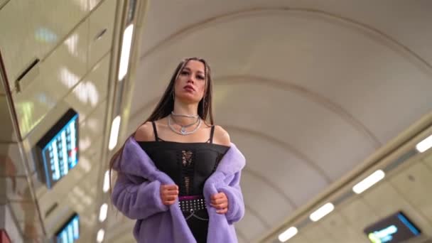 Menina modelo de moda em casaco de pele sintética roxo desnudou seus ombros andando em metro ou metrô plataforma em câmera lenta. Feminino com maquiagem de luxo, cabelo longo em roupa elegante. Vídeo FHD — Vídeo de Stock