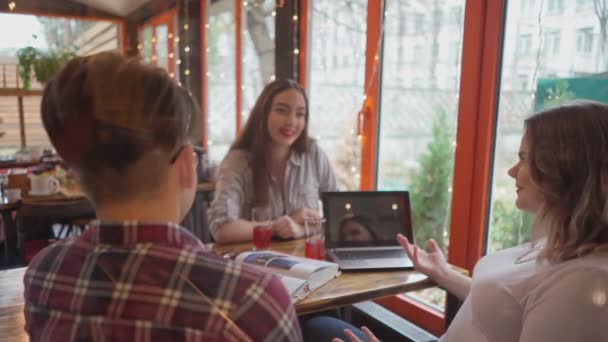 Tre studenter kille och flickor har diskussion medan du studerar sitter i ett café med lampor som körs på bakgrunden när de sitter vid ett bord med olika böcker på det. 4K-bilder — Stockvideo