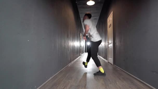 Jeune homme danseur hip hop contemporain dansant dans un rayon de lumière dans un long couloir sombre avec beaucoup de portes blanches des deux côtés. Images 4K — Video