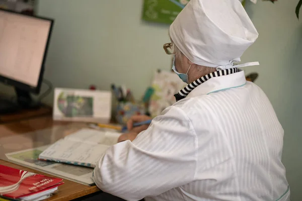 Senior doctor works with papers with a computer in foreground. Work of doctors team in ophthalmologist office. Mature female doctor writes medical forms. City Hospital. May, 2020, Brovary, Ukraine — Stock Photo, Image