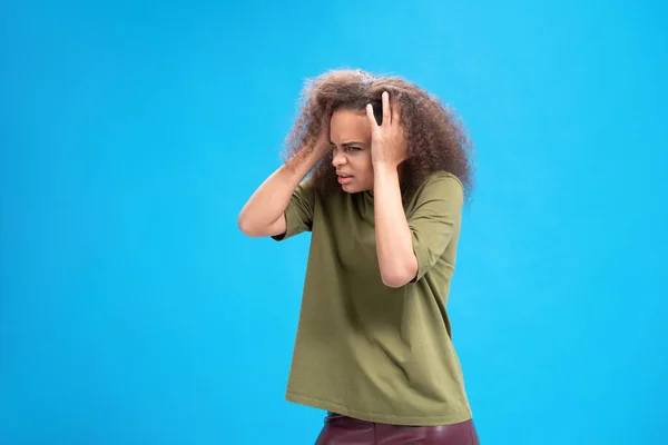 Éprouver migraine ou mal de tête afro-américaine jeune femme debout tenant la tête avec les mains en t-shirt olive isolé sur fond bleu. Concept des émotions humaines — Photo